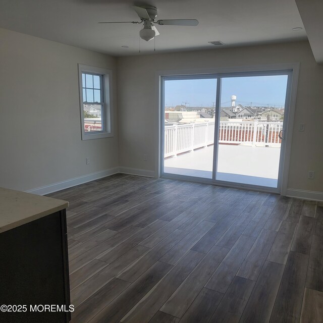interior space featuring baseboards, ceiling fan, dark wood-style floors, and visible vents