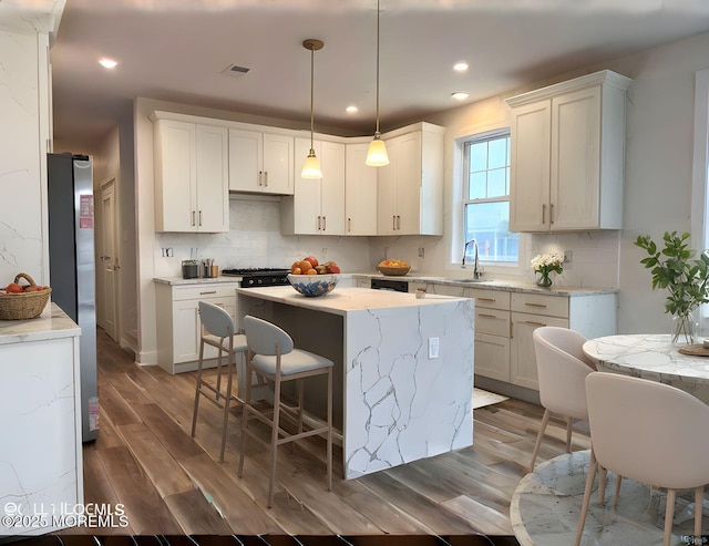 kitchen featuring a kitchen island, tasteful backsplash, wood finished floors, recessed lighting, and white cabinetry