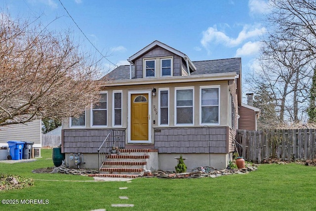 view of front of home featuring entry steps, a front yard, fence, and a shingled roof