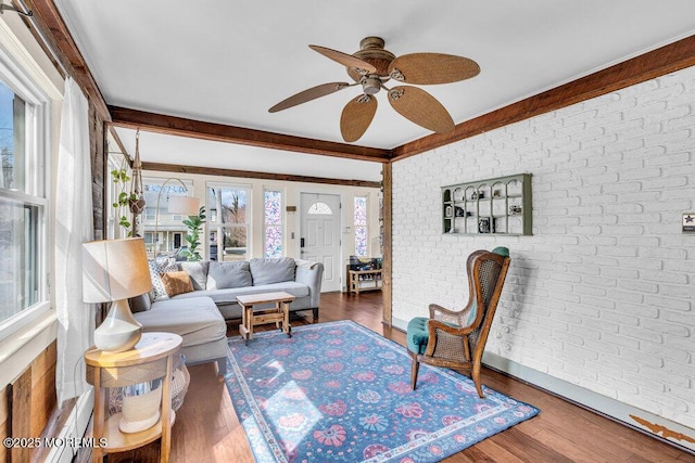 living room featuring beamed ceiling, wood finished floors, brick wall, and a ceiling fan