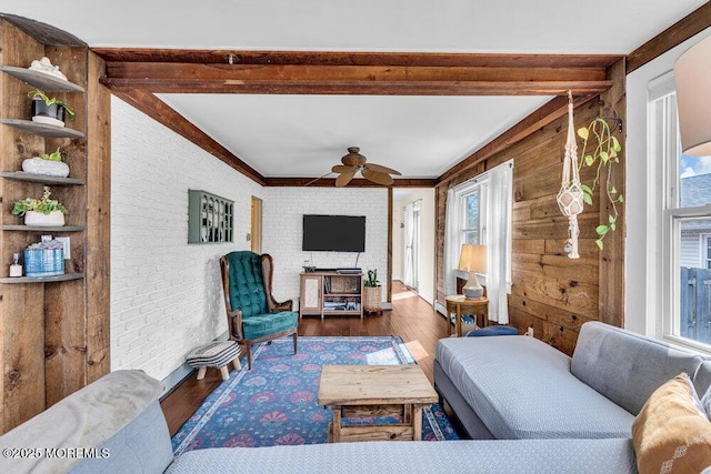 living room featuring beam ceiling, brick wall, wood finished floors, and a ceiling fan