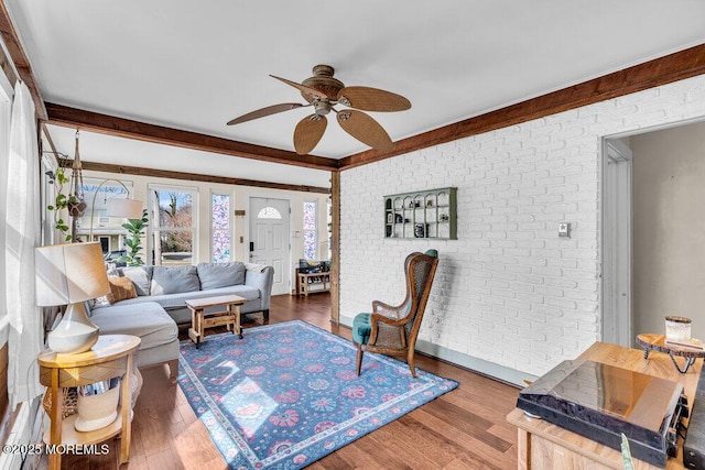 living area with a ceiling fan, wood finished floors, and brick wall