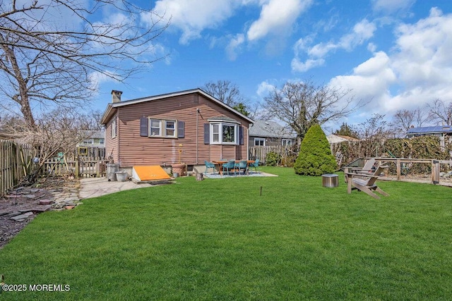 rear view of house featuring a patio area, a fenced backyard, a lawn, and a chimney