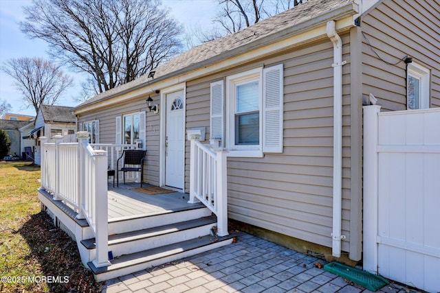 entrance to property featuring roof with shingles and a wooden deck