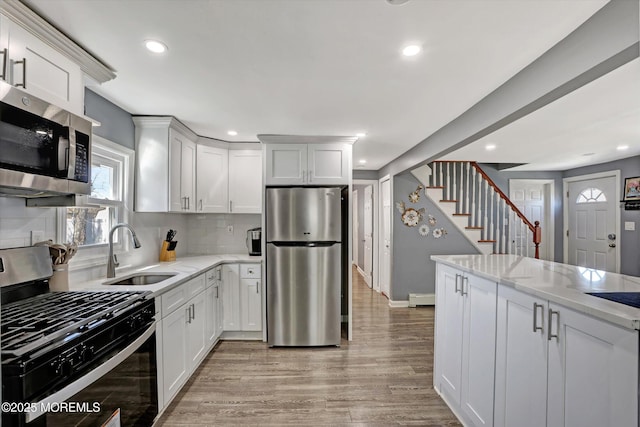 kitchen featuring light stone countertops, light wood-style flooring, a sink, appliances with stainless steel finishes, and backsplash