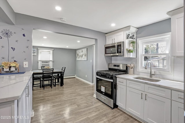 kitchen featuring light wood finished floors, baseboard heating, white cabinets, stainless steel appliances, and a sink