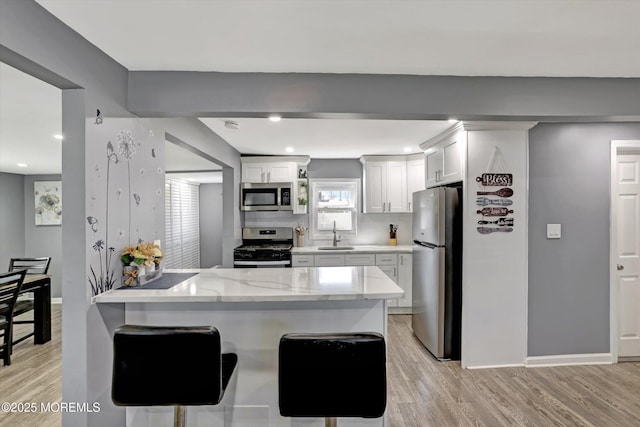 kitchen featuring white cabinets, appliances with stainless steel finishes, light wood-style floors, and a peninsula