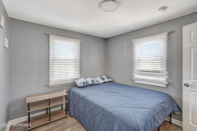 bedroom with multiple windows, wood finished floors, and baseboards