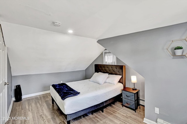 bedroom with a baseboard heating unit, lofted ceiling, baseboards, and wood finished floors