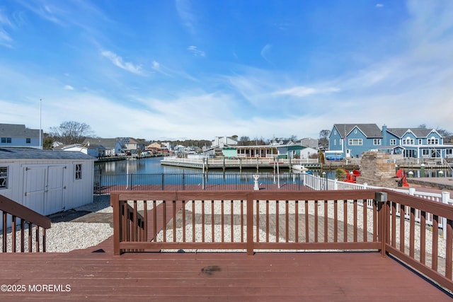 wooden deck featuring a water view, a residential view, a dock, an outdoor structure, and a storage unit