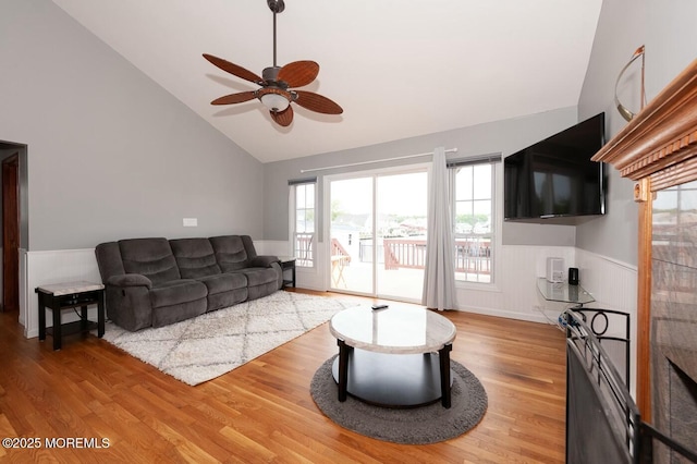 living area with high vaulted ceiling, a ceiling fan, wainscoting, and light wood finished floors