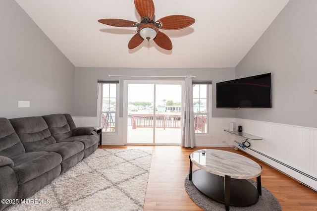 living room featuring a baseboard radiator, plenty of natural light, wainscoting, and vaulted ceiling