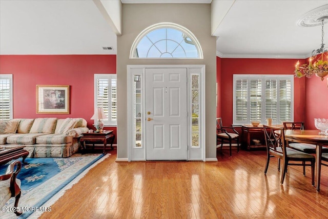 entrance foyer with visible vents, baseboards, ornamental molding, hardwood / wood-style floors, and an inviting chandelier