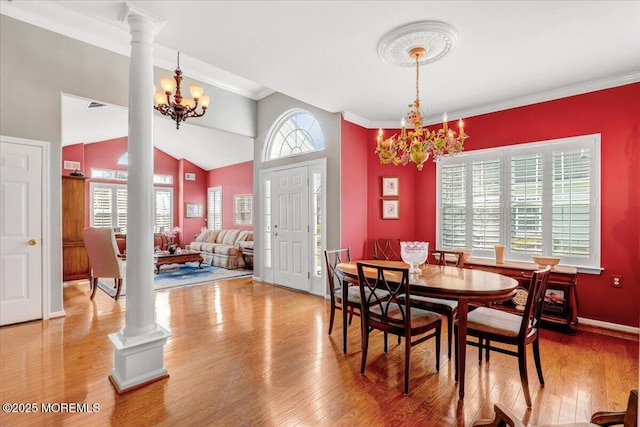 dining room with a notable chandelier, crown molding, ornate columns, and wood finished floors