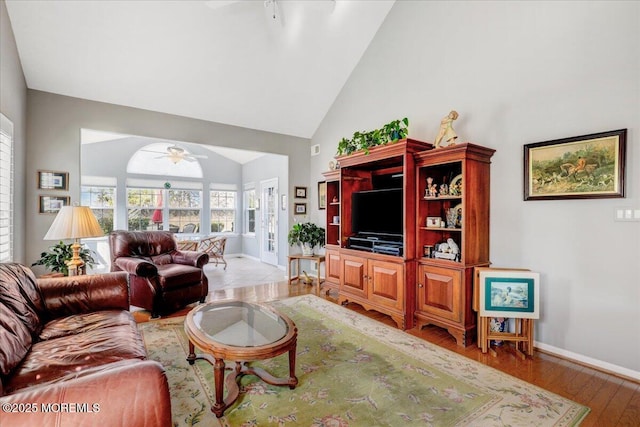 living room featuring light wood-style floors, baseboards, high vaulted ceiling, and a ceiling fan