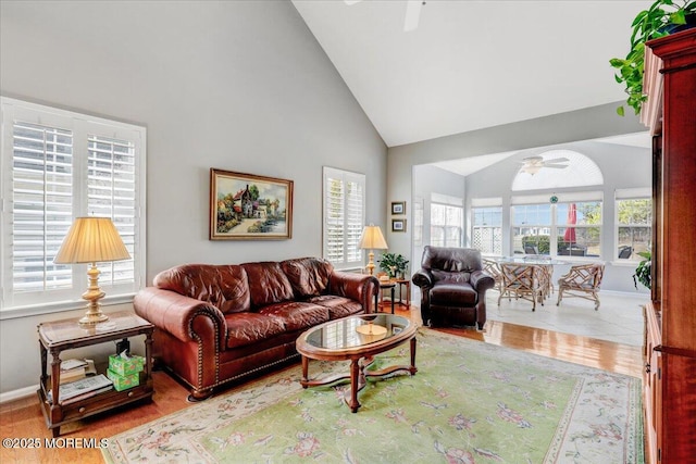 living area with wood finished floors, high vaulted ceiling, a healthy amount of sunlight, and ceiling fan