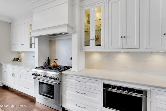 kitchen featuring glass insert cabinets, crown molding, custom exhaust hood, white cabinetry, and high end stainless steel range