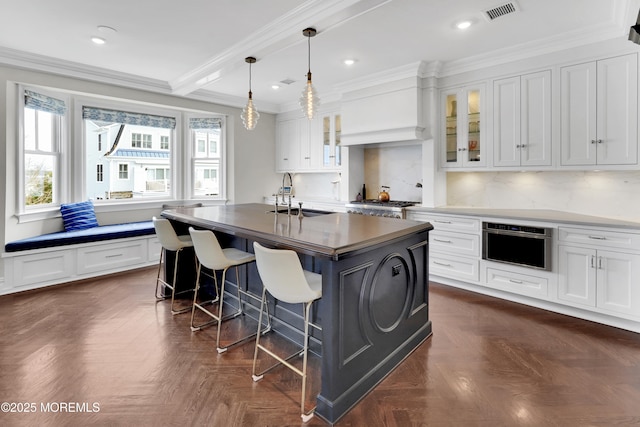 kitchen with visible vents, crown molding, a kitchen bar, custom range hood, and a sink