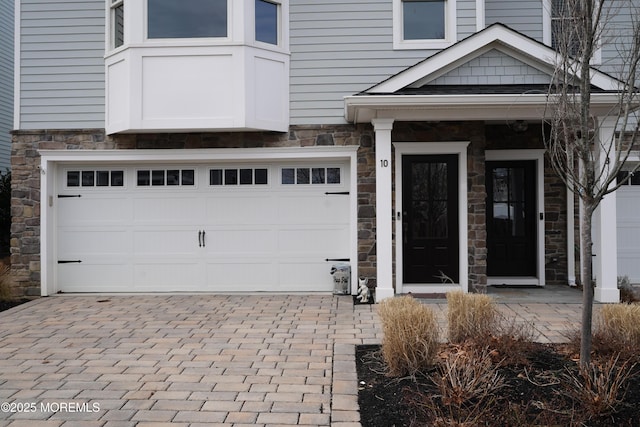 doorway to property featuring decorative driveway, stone siding, and a garage