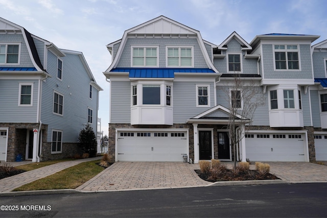 shingle-style home featuring stone siding, a gambrel roof, an attached garage, and decorative driveway