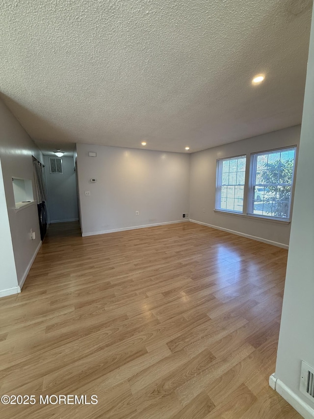 unfurnished room with visible vents, baseboards, light wood-style floors, and a textured ceiling