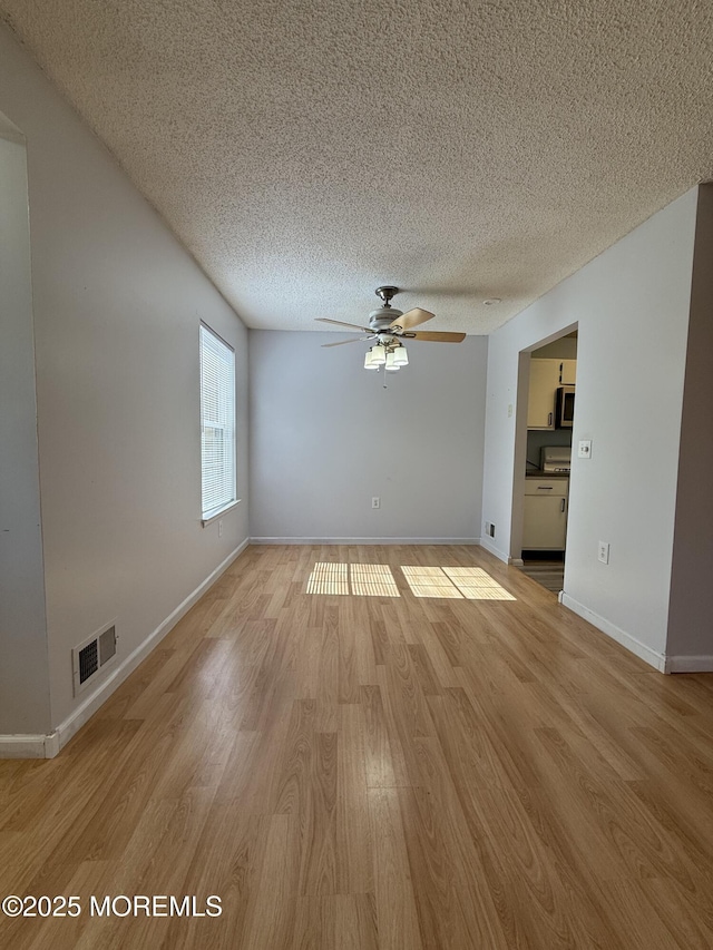 empty room featuring a ceiling fan, baseboards, visible vents, light wood-style floors, and a textured ceiling