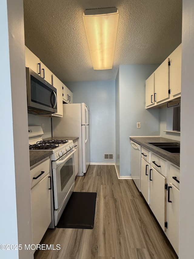 kitchen featuring white appliances, wood finished floors, visible vents, white cabinets, and dark countertops