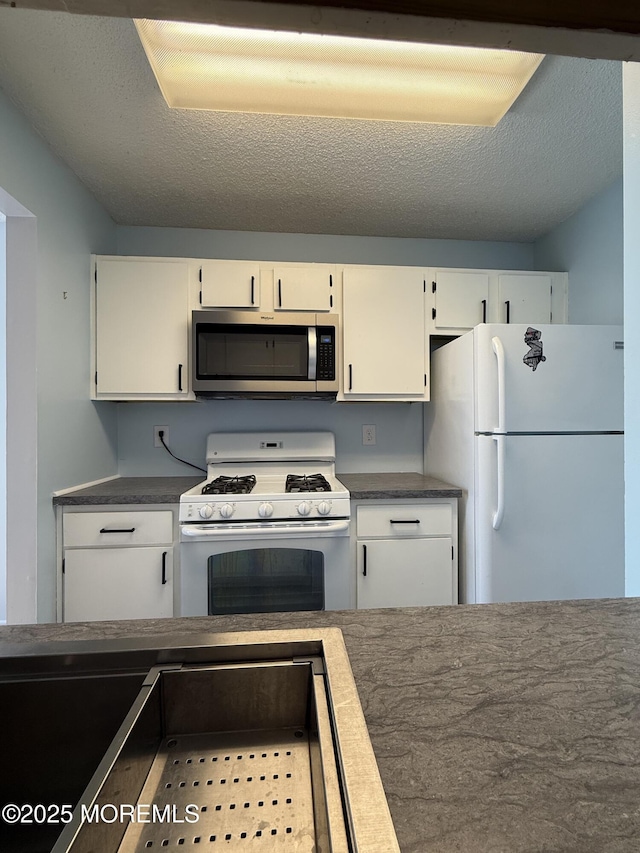 kitchen with a textured ceiling, white appliances, dark countertops, and white cabinetry