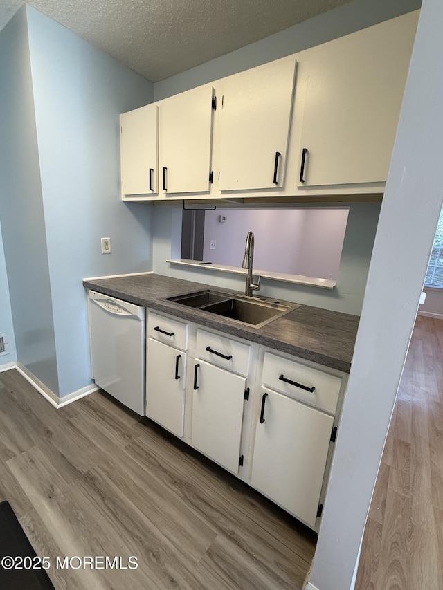 kitchen featuring dishwasher, dark countertops, light wood-style flooring, and a sink