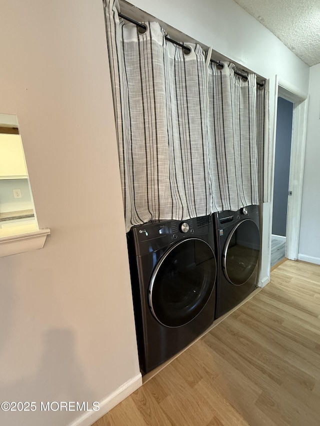 washroom with wood finished floors, baseboards, laundry area, a textured ceiling, and washing machine and dryer