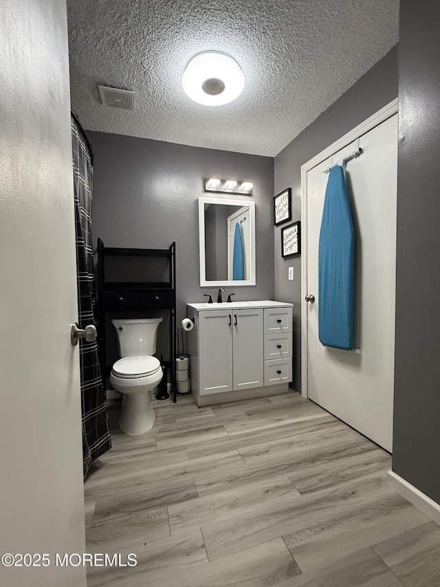 bathroom with visible vents, toilet, wood finished floors, and a textured ceiling