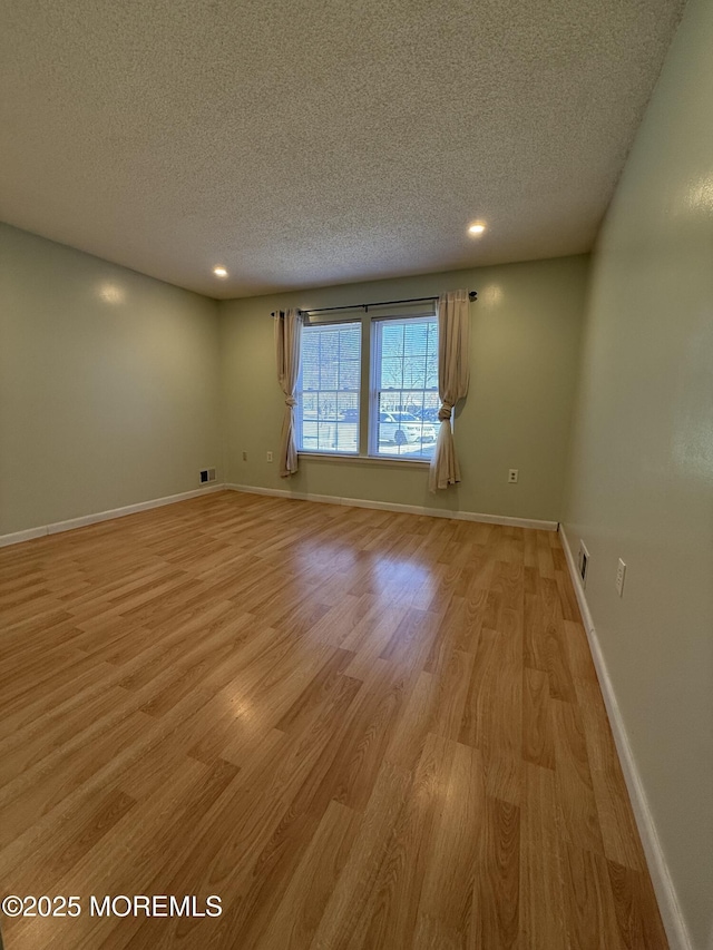 empty room with recessed lighting, light wood-style floors, baseboards, and a textured ceiling