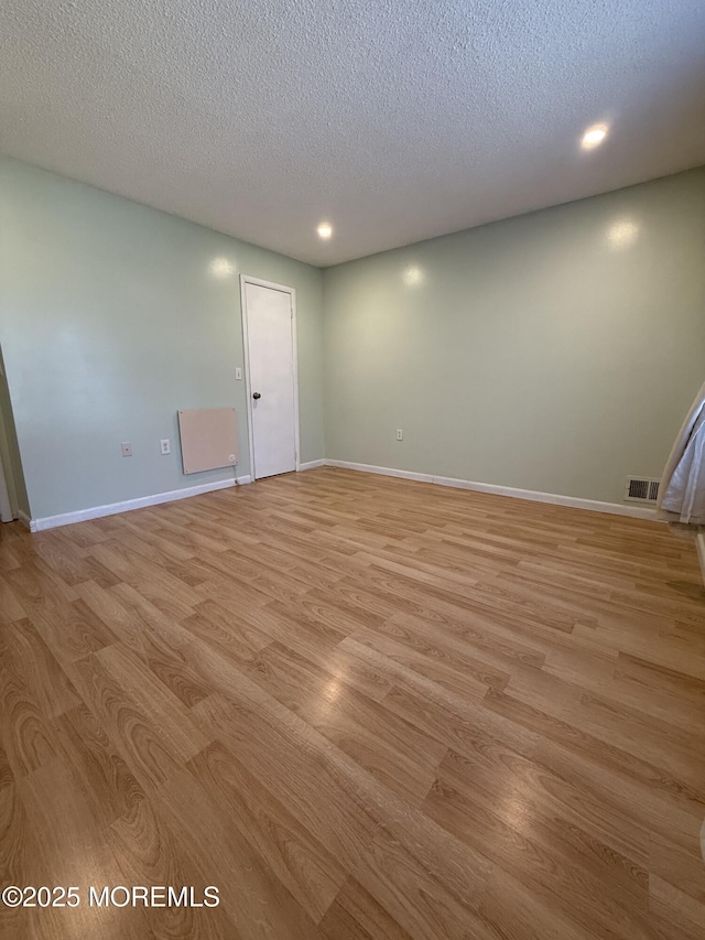 unfurnished room featuring visible vents, baseboards, a textured ceiling, and light wood finished floors