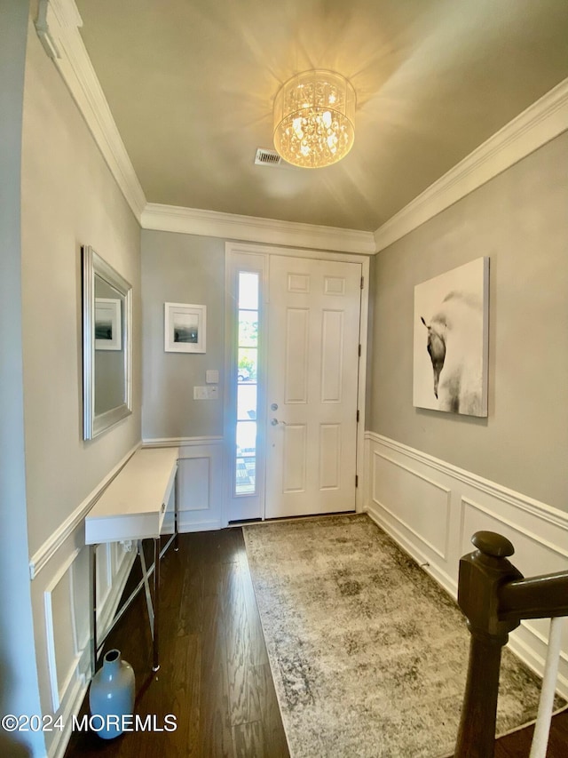 foyer with a decorative wall, crown molding, dark wood finished floors, wainscoting, and a notable chandelier