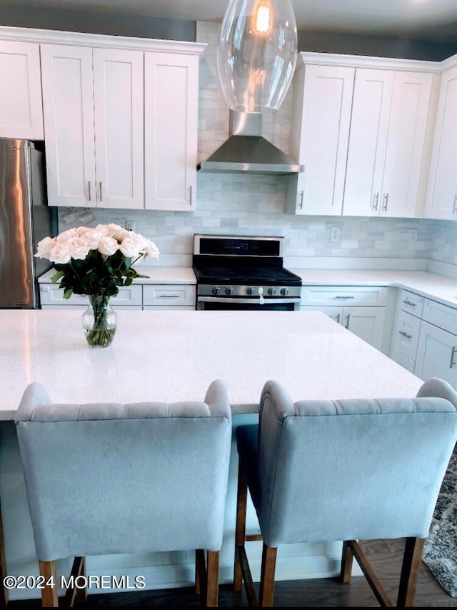 kitchen with backsplash, appliances with stainless steel finishes, white cabinetry, and wall chimney range hood