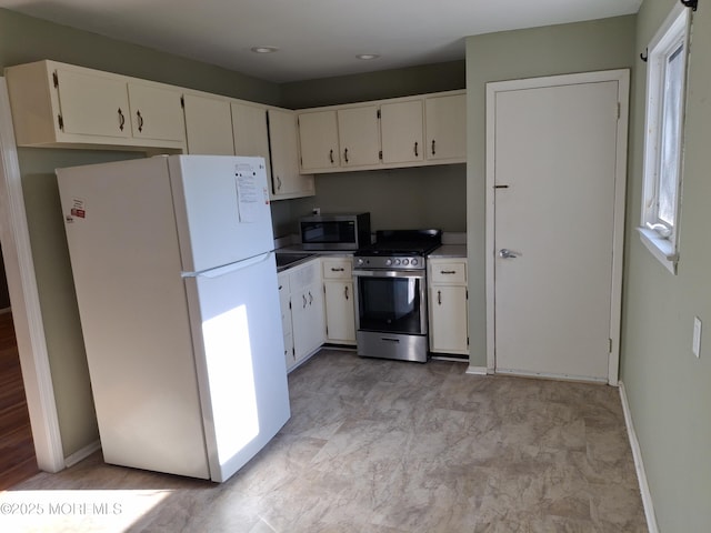 kitchen featuring baseboards, appliances with stainless steel finishes, and white cabinetry