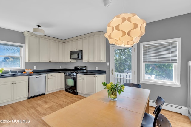 kitchen featuring dark countertops, light wood finished floors, black appliances, and a sink