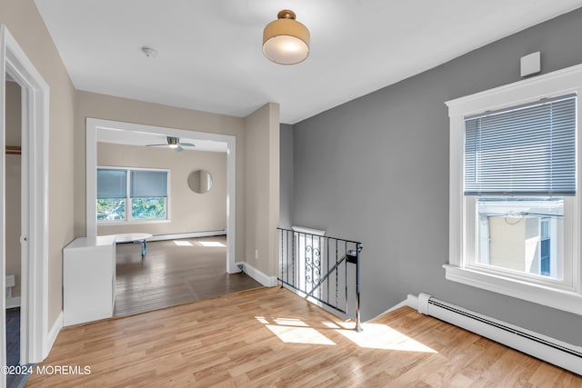 hall with wood finished floors, baseboards, a baseboard radiator, a baseboard heating unit, and an upstairs landing