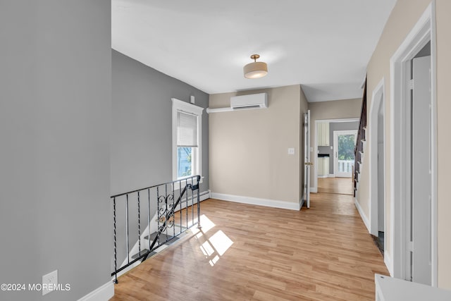 hall featuring an upstairs landing, light wood finished floors, a wall mounted air conditioner, and baseboards