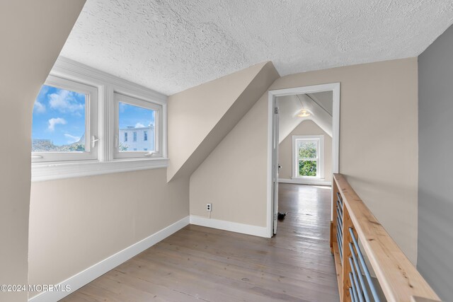 additional living space with hardwood / wood-style flooring, vaulted ceiling, baseboards, and a textured ceiling