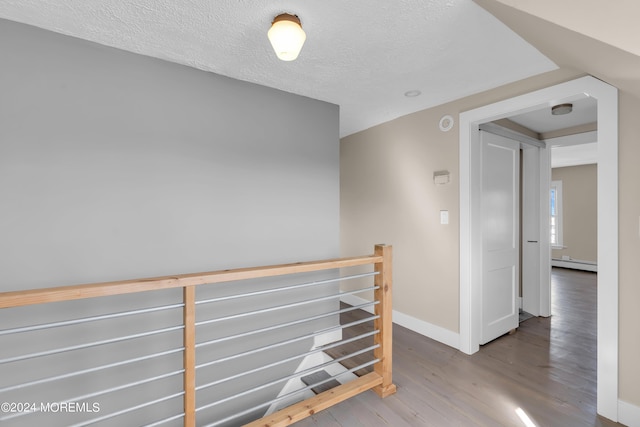 hallway with an upstairs landing, a textured ceiling, wood finished floors, baseboards, and baseboard heating