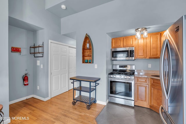 kitchen featuring light stone counters, stainless steel appliances, baseboards, and light wood-style flooring