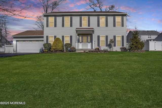 colonial home with aphalt driveway, a yard, fence, and a garage