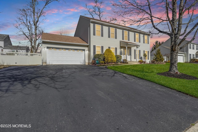 colonial home with driveway, a front yard, an attached garage, and fence