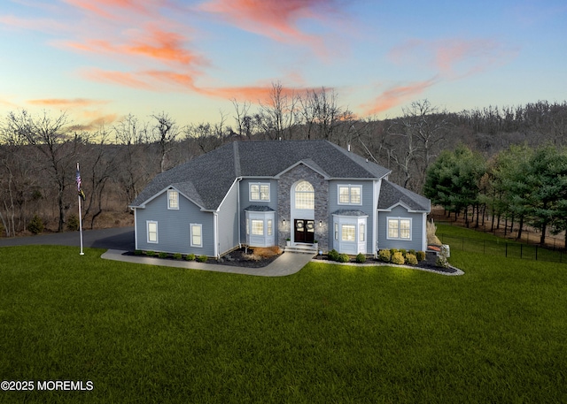 view of front of property featuring a front lawn, fence, stone siding, and a shingled roof