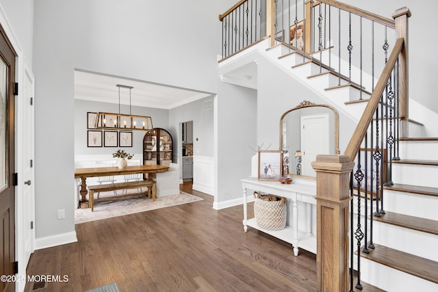 stairs featuring crown molding, baseboards, a towering ceiling, wood finished floors, and a notable chandelier