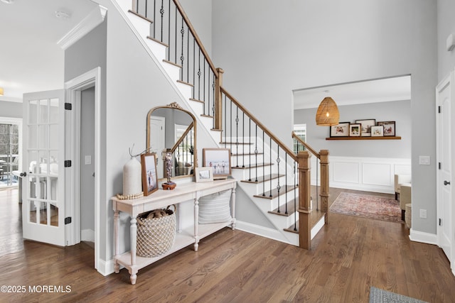 staircase featuring a decorative wall, wood finished floors, a towering ceiling, and ornamental molding