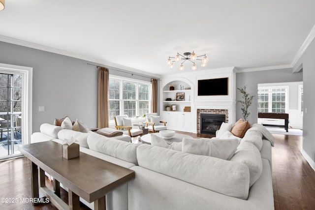 living room featuring built in shelves, crown molding, dark wood-type flooring, a chandelier, and a fireplace