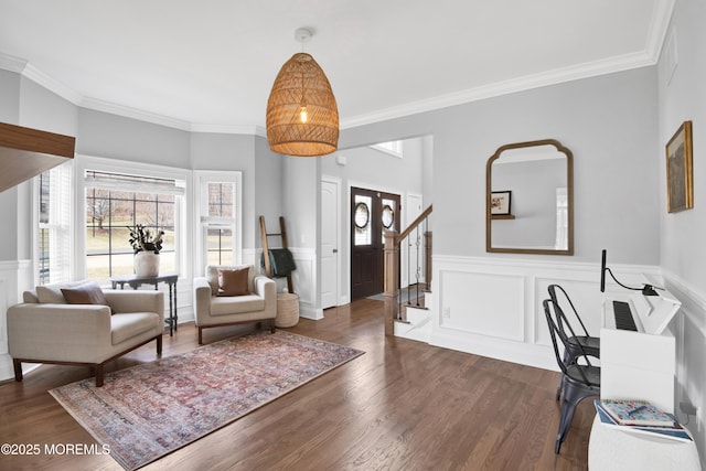 living area featuring stairs, a wainscoted wall, ornamental molding, and dark wood-style flooring