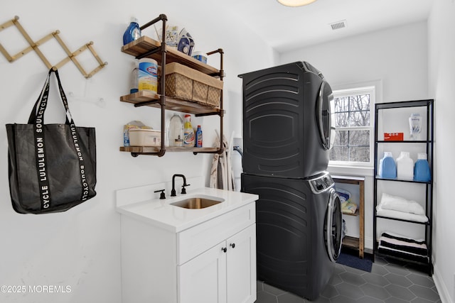 laundry area featuring stacked washer / dryer, visible vents, dark tile patterned floors, cabinet space, and a sink